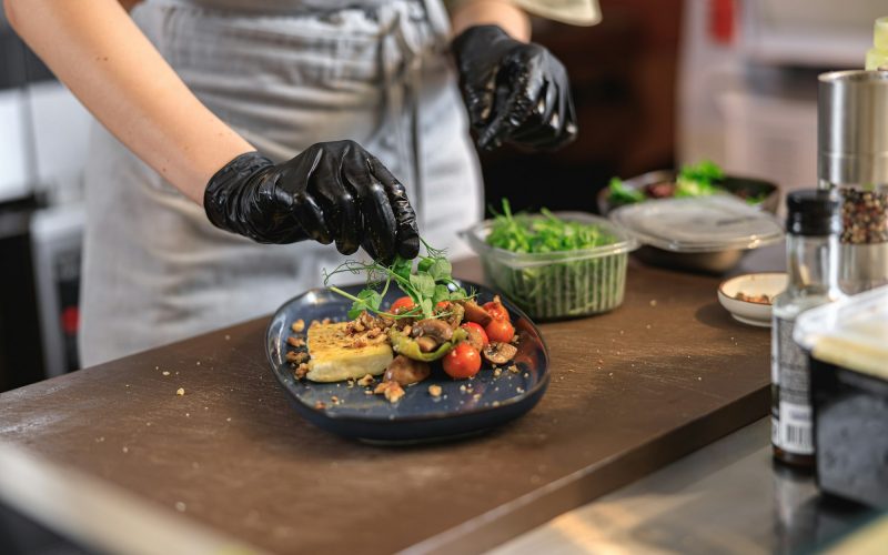 Professional chef is decorating ready meal with greens on restaurant kitchen